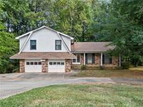 Charming split-level home featuring a two-car garage and partially bricked exterior with lots of mature trees at 235 Shallowford Nw Rd, Kennesaw, GA 30144