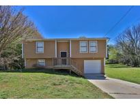 Split-level home featuring a front porch, attached garage and well-maintained lawn under a sunny blue sky at 5219 Sweet Air Ln, Stone Mountain, GA 30088