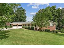 Charming brick home featuring a two-car garage, well-maintained lawn, and lush greenery at 4135 Shoshone Valley Rd, Marietta, GA 30068