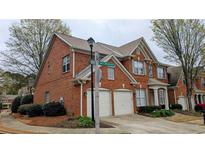 Charming brick townhome featuring a two-car garage, well-maintained landscaping and architectural roof details at 401 Wellwood Way, Roswell, GA 30075