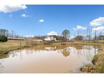 Scenic pond view reflecting a beautiful country home with mature trees under a bright blue sky at 2442 Lower Union Hill Rd, Canton, GA 30115