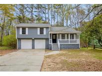 Charming split-level home with a two-car garage, covered porch, and gray siding nestled among mature trees at 175 Montego Cir, Riverdale, GA 30274