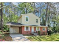 Charming two-story home features a brick facade, light yellow siding, and a covered carport in a lush, green setting at 3052 Sw Highbury Sw Trl, Atlanta, GA 30354