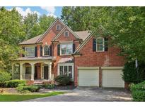 Charming brick home with a welcoming front porch and a two-car garage nestled among mature trees at 8355 Ainsworth Dr, Cumming, GA 30041
