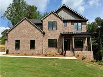 Beautiful brick two-story home with black trim windows, a covered porch, and lush green lawn at 6120 Hutchins Dr, Buford, GA 30518
