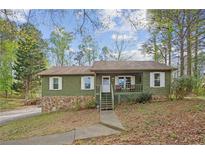 Charming single-story home featuring a stone foundation and inviting front porch, nestled among mature trees at 6909 Heritage Pl, Acworth, GA 30102