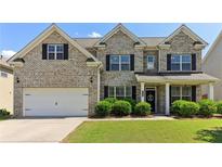 Charming brick two-story home featuring a manicured lawn, two car garage, and welcoming front porch at 7130 Ansley Park Way, Cumming, GA 30028