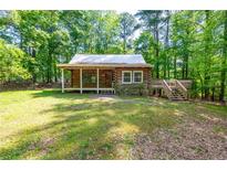 Rustic log cabin with a metal roof and a covered front porch nestled among the trees at 1615 Hilltop Ct, Woodstock, GA 30188