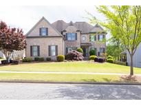 Inviting brick home boasts a manicured lawn, beautiful landscaping, and charming architectural details at 5081 Stone Moss Way, Hoschton, GA 30548