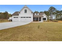 Beautiful white farmhouse-style home with a three-car garage and a large, sloping front lawn and mature landscaping at 4025 Bullock Bridge Rd, Loganville, GA 30052