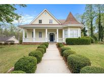 Charming yellow two-story home featuring a manicured lawn, front porch, and unique architectural details at 5732 Falls View Dr, Buford, GA 30518