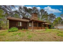 Rustic wood home with a covered porch, stone foundation, and mature trees surrounding the property at 2140 Teri Ln, Conyers, GA 30013