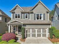 Charming two-story home with gray siding, stone accents, a two-car garage, and professional landscaping at 8385 E Village School E Dr, Cumming, GA 30041