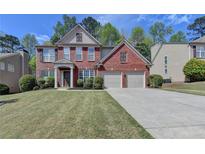 Charming two-story brick home with a well-manicured lawn and two-car garage on a sunny day at 580 Hammersmith Dr, Suwanee, GA 30024
