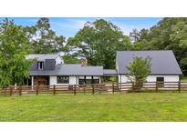 Beautiful modern farmhouse with black metal roof and white siding surrounded by lush greenery and a wooden fence at 85 Carroll Slough Rd, Kingston, GA 30145