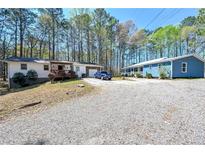 Exterior shot of two homes with mature trees and gravel driveway on a sunny day at 5955 Kemp Dr, Acworth, GA 30102