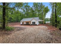 Charming, newly built single-story home with light gray roof, light siding and gravel driveway surrounded by trees at 1765 Harmony Rd, Temple, GA 30179