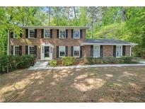 Charming two-story brick home with black shutters and a well-manicured front lawn in a wooded lot at 5145 Davantry Dr, Dunwoody, GA 30338