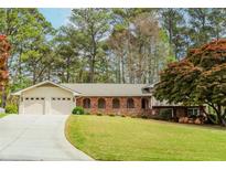Charming single story brick home with a well-manicured lawn, mature trees, and attached two-car garage at 1152 Old Coach Rd, Stone Mountain, GA 30083