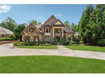 Beautiful brick and stone home featuring a covered front porch, manicured lawn, and curved driveway at 6935 Wakehurst Pl, Cumming, GA 30040