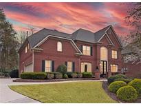 Stunning two-story brick home featuring manicured lawn and a warm, inviting facade at sunset at 9250 Nesbit Lakes Dr, Alpharetta, GA 30022