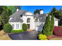 Elegant white home featuring arched windows, manicured landscaping, and a paved driveway at 7080 Greatwood Trl, Alpharetta, GA 30005