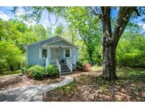 Charming blue cottage with white trim, inviting front porch, and lush landscaping with a large tree at 8211 Thompson St, Douglasville, GA 30134