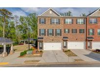 Three-story brick townhome featuring an attached garage and well-maintained landscaping with a gazebo in the background at 2042 Clay Rd, Snellville, GA 30078