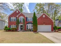 Charming two-story red brick home featuring a well-manicured lawn, shutters, and attached two car garage at 725 Martin Field Dr, Lawrenceville, GA 30045