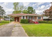 Charming brick home featuring a well-maintained lawn, covered carport, and landscaped front yard at 5295 Woodland Dr, Lake City, GA 30260