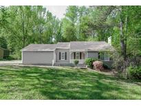 Charming single-story home featuring a covered front porch and surrounded by lush trees and green lawn at 2374 Rolling Acres Sw Dr, Conyers, GA 30094