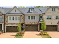 Charming townhome exterior featuring mixed brick and stone facade with well-manicured landscaping and attached garages at 126 Abbington River Ln, Atlanta, GA 30339