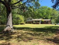 Sprawling front yard with a two-story home nestled among mature trees and established landscaping at 3418 Johnson Dr, Snellville, GA 30039