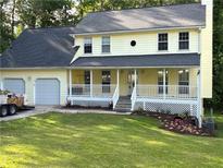 Charming yellow two-story home with a covered front porch, a two-car garage, and a lush green lawn at 3899 Leach Rd, Snellville, GA 30039
