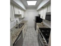 Galley kitchen featuring stainless steel appliances, granite countertops, and neutral gray tile flooring at 6851 Roswell Rd # O10, Atlanta, GA 30328
