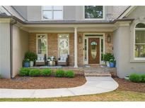 Charming covered porch with stone accents, seating area, and a welcoming front door at 1315 Woodland Trce, Cumming, GA 30041