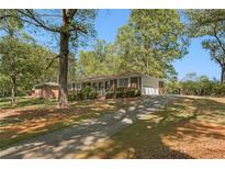 Charming brick home featuring a long driveway and mature trees on a sunny day at 1788 Hammond Woods Sw Cir, Marietta, GA 30008