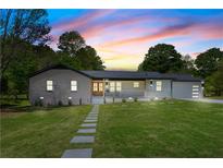 Charming single-story home featuring a brick facade, manicured lawn, and inviting walkway under a colorful sunset sky at 5036 Chestnut Forest Ln, Dunwoody, GA 30360