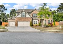 Two-story brick home featuring a three car garage and a beautifully landscaped front yard at 1304 Slate Bend Dr, Dacula, GA 30019