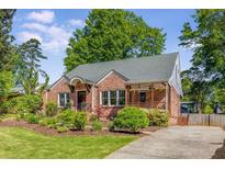 Charming brick home featuring a well-manicured lawn, mature trees, and welcoming front porch at 1256 Spring Valley Ne Ln, Atlanta, GA 30306