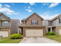 Two-story tan home featuring a brick garage and manicured landscaping at 5885 San Gabriel Ln, Atlanta, GA 30349