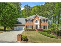 Charming two-story brick home with manicured lawn and lush landscaping in a wooded suburban setting at 815 Kings Arms Way, Alpharetta, GA 30022