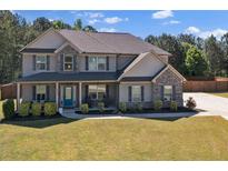 Two-story home featuring a manicured lawn, gray siding, stone accents, and a welcoming covered front porch at 524 Trousseau Ln, Mcdonough, GA 30252