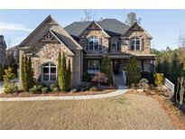 Beautiful stone home features a manicured lawn and mature evergreens highlighting the architectural details at 12640 Hearthstone Way, Alpharetta, GA 30009
