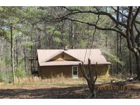 Charming exterior view of home with metal roof, wood siding and covered side porch surrounded by mature trees at 8740 Atlanta Newnan Rd, Chattahoochee Hills, GA 30268
