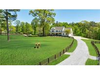 Stunning farmhouse on sprawling green lawn with fenced pasture and horses under a bright blue sky at 1200 Old Lathemtown Rd, Canton, GA 30115