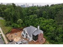 New construction home with gray roof and brick accents surrounded by lush green trees and a city skyline in the background at 469 Emily Reed Lot 11 Ln, Atlanta, GA 30342