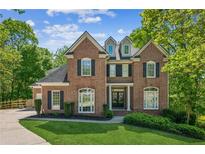 Elegant two-story brick home featuring dormer windows, a manicured lawn, and lush landscaping at 4750 Spring Wood Trce, Cumming, GA 30041