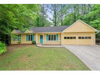 Charming yellow ranch-style home with a two-car garage, a manicured lawn and trees in the background at 502 Knollwood Pl, Woodstock, GA 30188