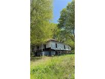 An exterior shot of a white, weathered home surrounded by trees and an overgrown yard at 6648 Ridge Ave, Douglasville, GA 30134